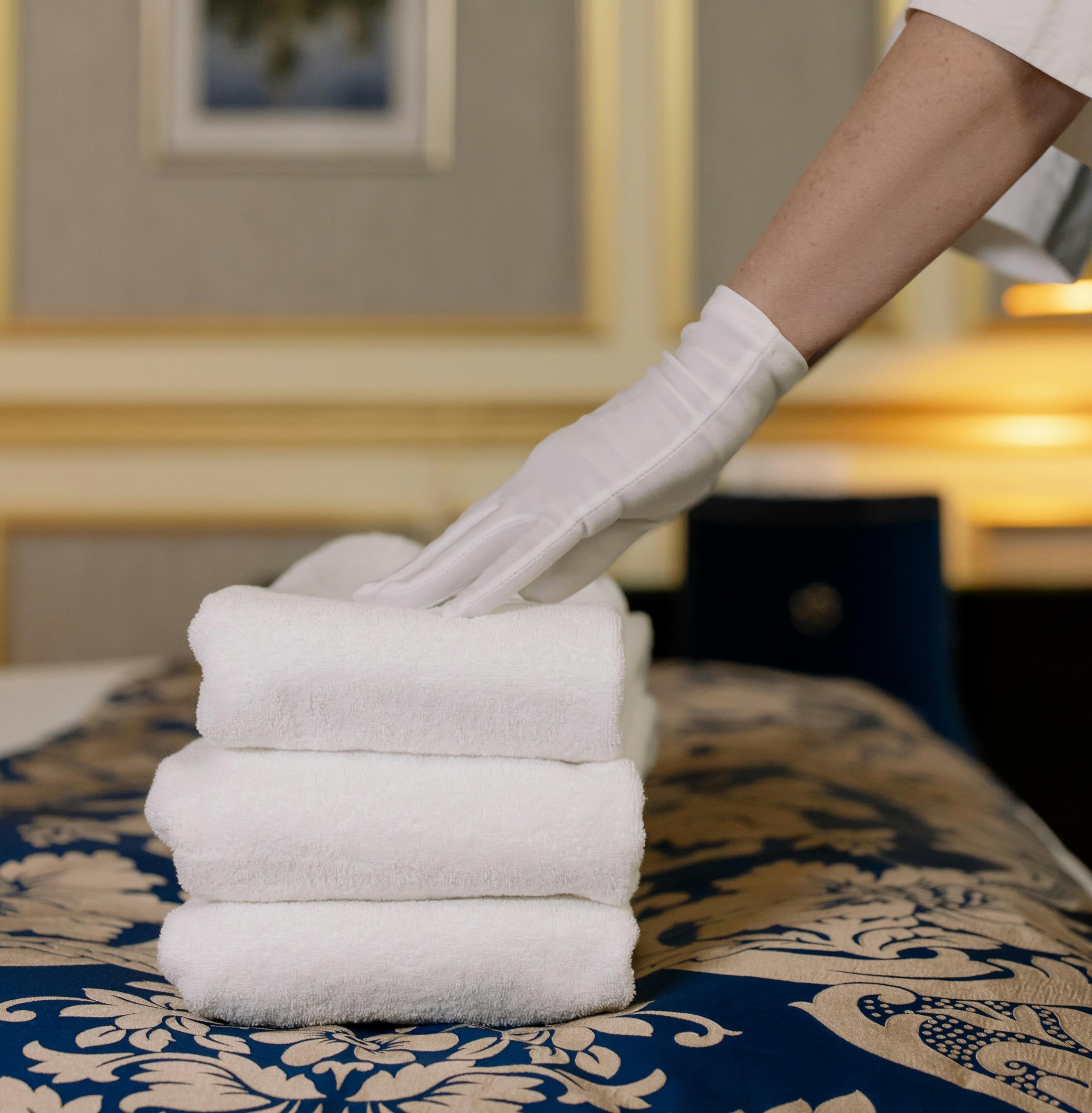 Hotel linen service — white-gloved housekeeper placing folded towels on a luxury hotel bed